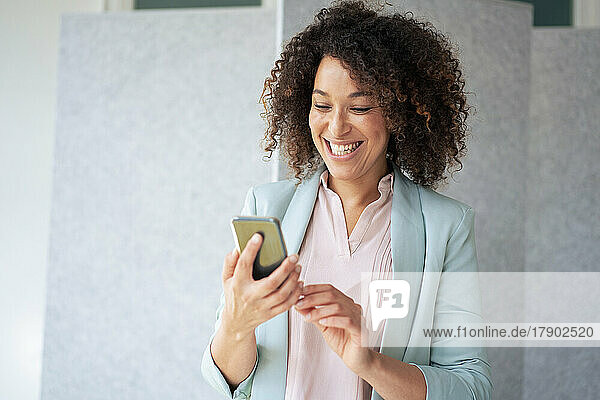 Cheerful businesswoman using mobile phone at office