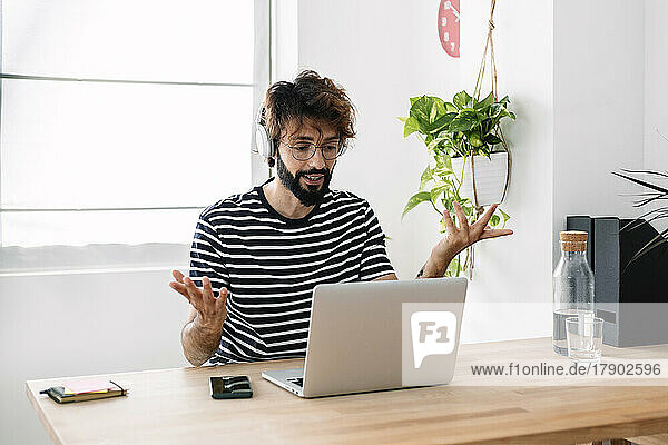 Freelance wearing wireless headphones gesturing on video call through laptop