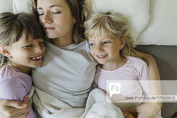 Lächelnde Geschwister entspannen sich mit der Mutter zu Hause im Bett