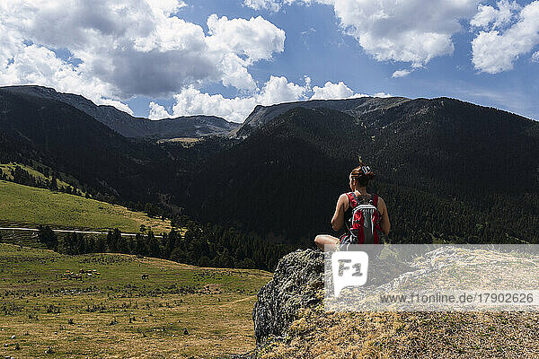 Woman with backpack sitting in front of mountain