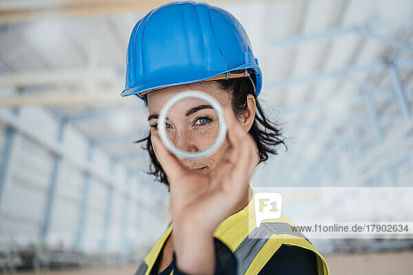 Smiling engineer looking through ring shape object in factory