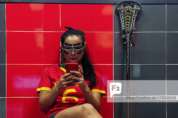 Lacrosse-Spieler schreibt Textnachrichten per Smartphone  während er in der Umkleidekabine sitzt