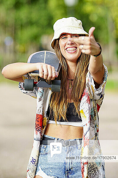 Cheerful woman with skateboard showing middle finger