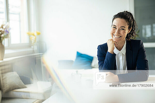 Smiling businesswoman sitting with hand on chin