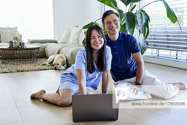 Happy freelancers with laptop sitting on floor in living room at home