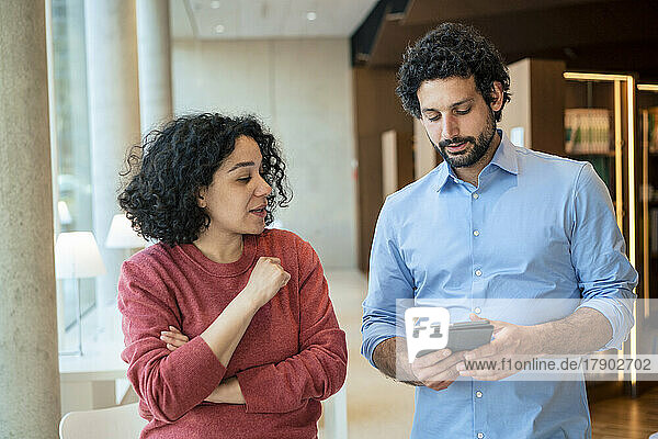 Man and woman discussing over tablet PC in library