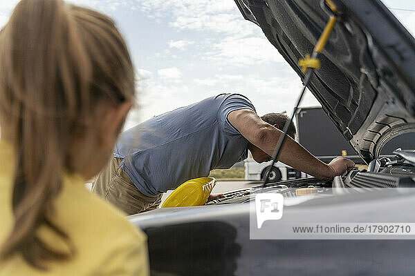 Mature man repairing car in front of girl at parking lot