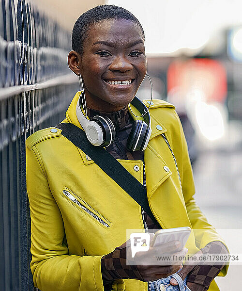 Junge Frau in Lederjacke hält Smartphone am Zaun