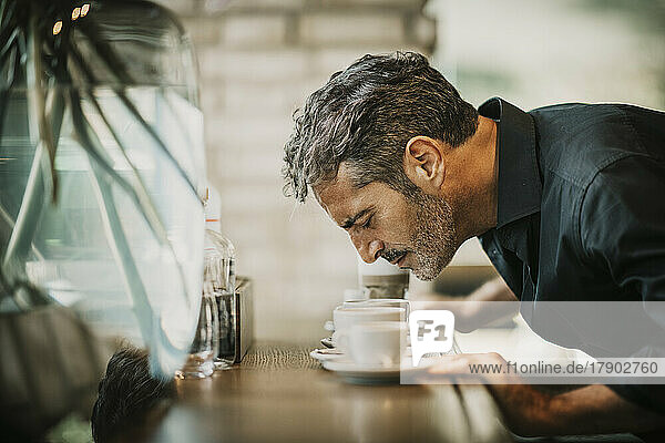 Reifer Mann riecht Kaffee auf dem Tisch im Café