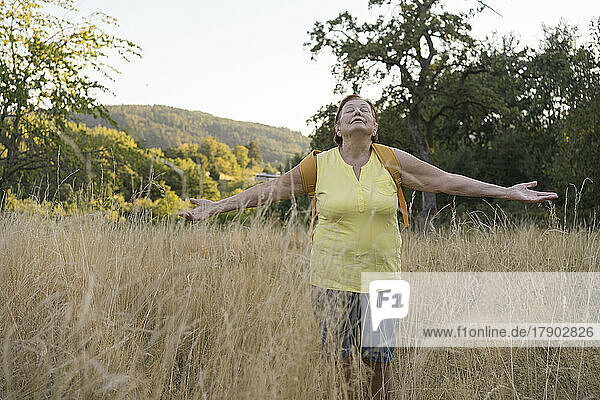 Senior woman with arms outstretched standing in field