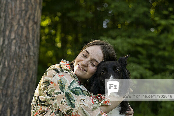 Happy young woman embracing dog in park