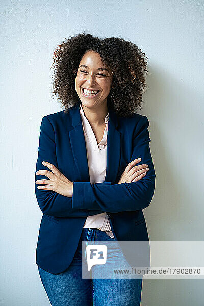Businesswoman with arms crossed laughing in front of wall
