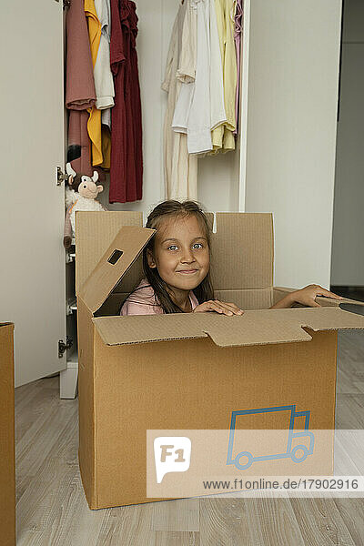 Smiling girl sitting in cardboard box at home