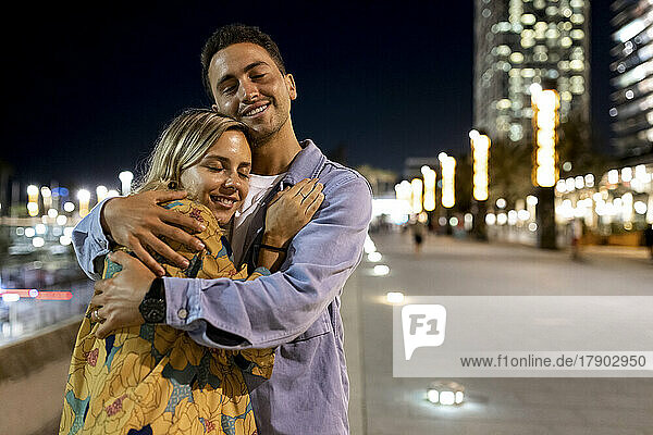 Lächelndes junges Paar mit geschlossenen Augen  das sich nachts umarmt