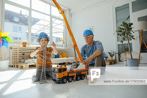 Junge imitiert als Ingenieur  der mit seinem Großvater zu Hause ein Strommastmodell an einem Spielzeugkran befestigt