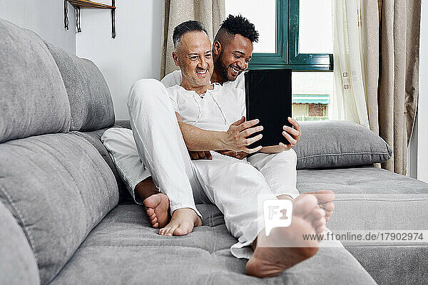 Reifer Mann benutzt Tablet-PC und sitzt mit seinem Freund zu Hause auf dem Sofa