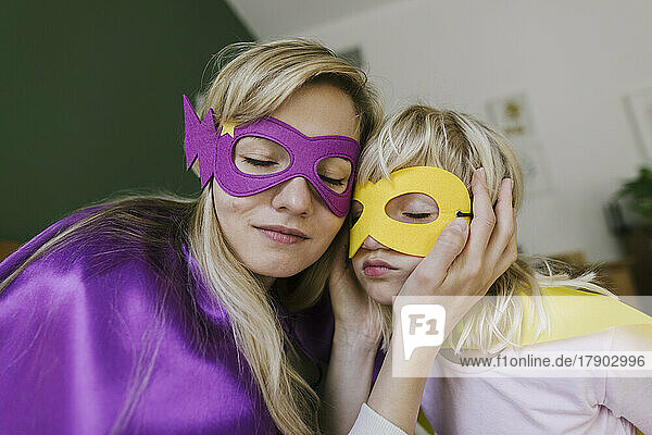 Mutter und Tochter mit geschlossenen Augen tragen Maske und Umhang zu Hause