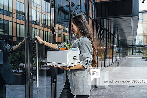 Smiling businesswoman with box opening glass door