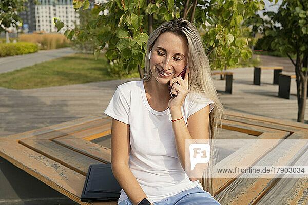 Happy young woman talking on smart phone in park