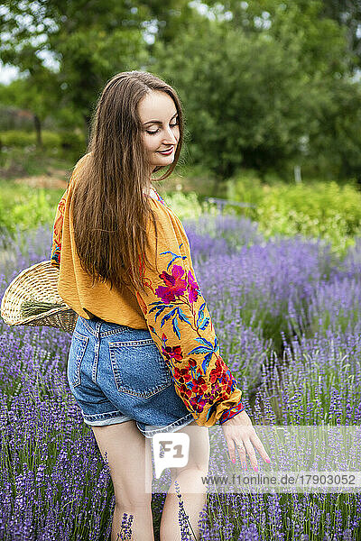 Happy woman with basket touching lavender flower plants at field