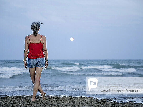 Frau schaut vom Strand aus auf den Mond