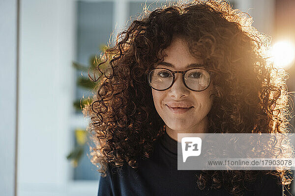 Lächelnde junge Frau mit lockigem Haar und Brille