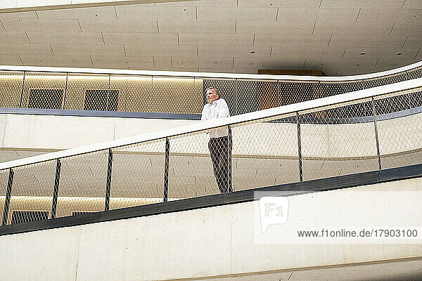Senior businessman leaning on railing in office corridor