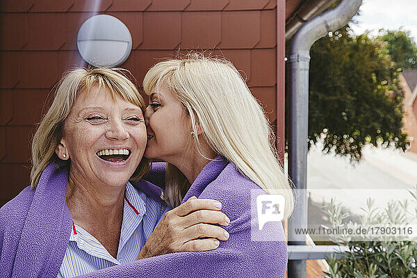 Blonde Frau küsst Mutter auf die Wange  die auf dem Balkon steht