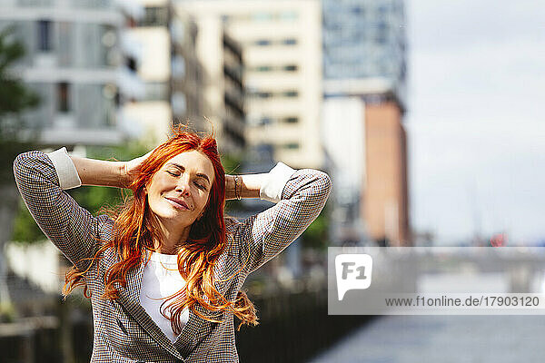 Happy redhead woman with eyes closed standing at Hafencity
