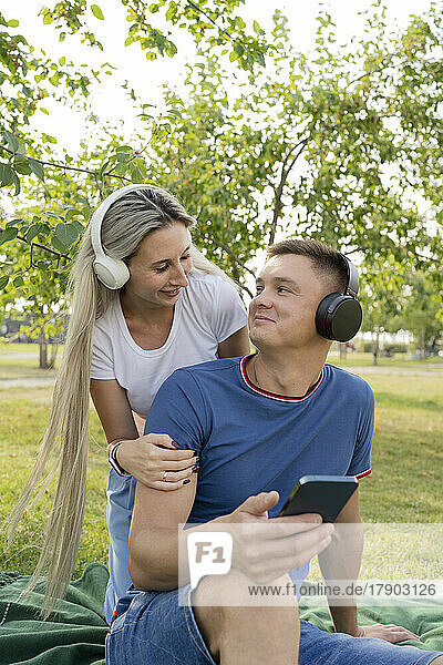 Young couple wearing headphones listening to music in park