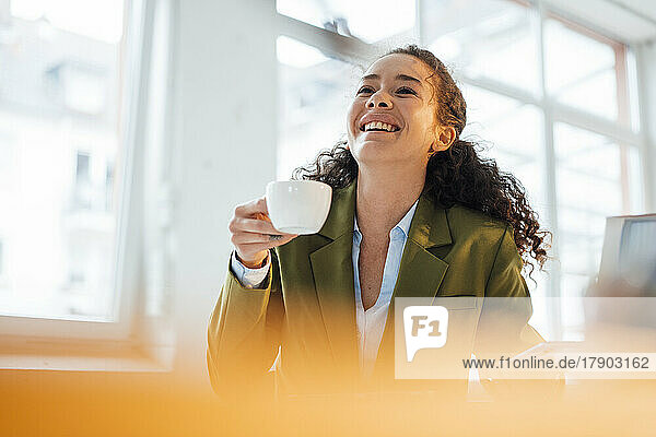 Fröhliche junge Geschäftsfrau hält Kaffeetasse im Büro