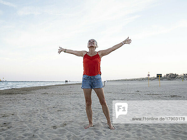 Senior woman with arms outstretched standing at beach