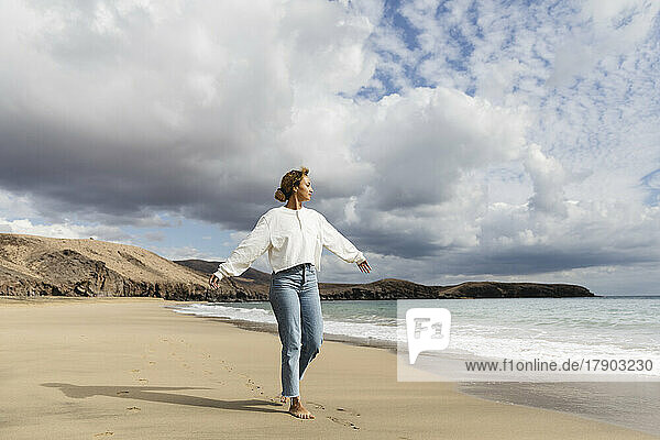 Young woman walking with arms outstretched at beach on sunny day