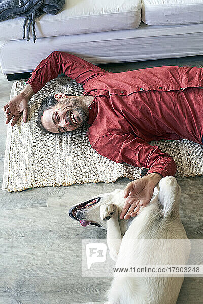 Happy man and dog lying on floor at home