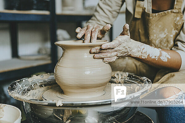 Hands of craftswoman molding pot shape on pottery wheel