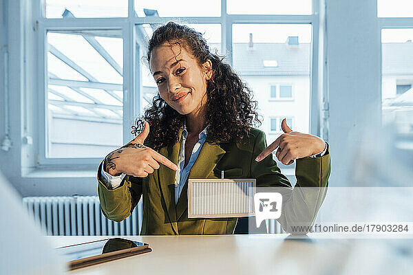 Smiling young businesswoman pointing at solar panel at desk
