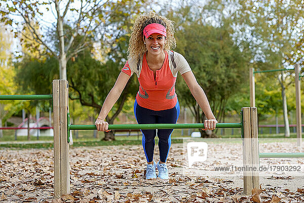 Happy sportswoman practicing push-ups on horizontal bar at park