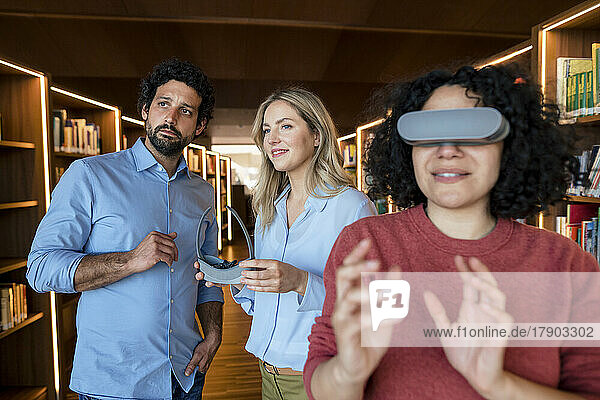 Gemischtrassige Kollegen mit VR-Brille in beleuchteter Bibliothek
