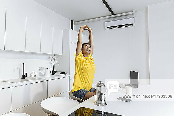 Happy woman stretching in kitchen taking a break fron freelance work
