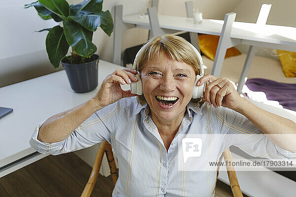 Cheerful senior woman listening music through wireless headphones