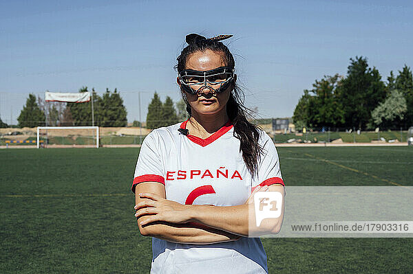 Player wearing protective eyewear standing with arms crossed on lacrosse field