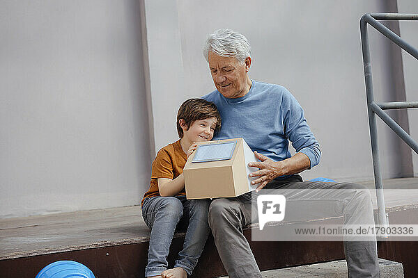 Grandfather and grandson looking at solar house model sitting on steps