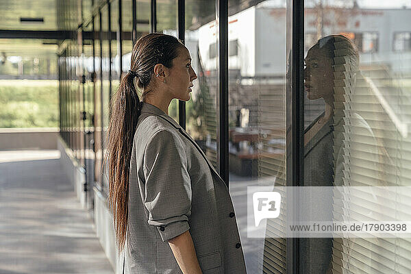 Businesswoman with long hair looking at reflection on glass wall