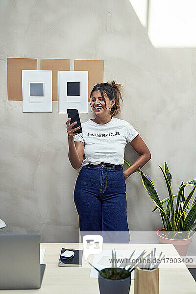 Smiling businesswoman using smart phone leaning on wall