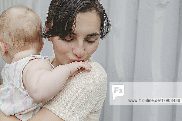Mother kissing baby girl's little hand in front of wall