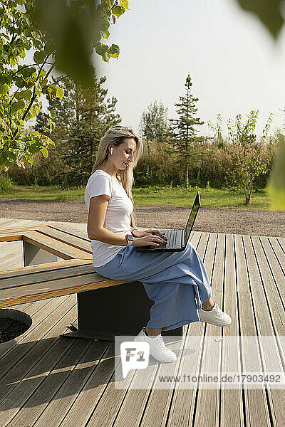 Freelancer working on laptop sitting on bench in park