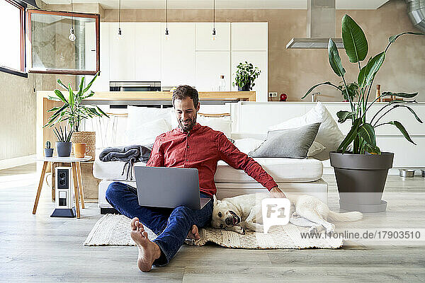 Freelancer sitting with laptop and petting his dog