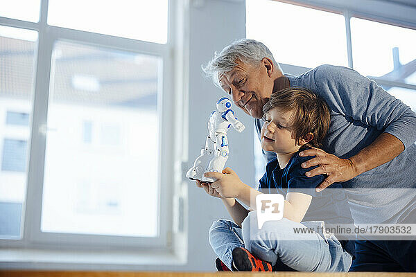 Smiling senior man by grandson with robot model at home