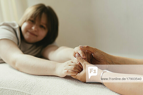 Smiling woman holding hands with mother on sofa at home