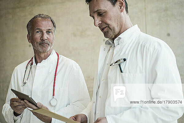 Senior doctor with tablet PC by colleague looking at file in hospital